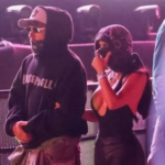 Lewis Hamilton wearing black Bieberchella hoodie, cap, sunglasses and face bandana standing next to Kim Kardashian in low cut black halter top with her face wrapped in a scarf at Coachella 2026 during Justin Bieber concert