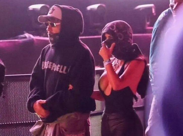 Lewis Hamilton wearing black Bieberchella hoodie, cap, sunglasses and face bandana standing next to Kim Kardashian in low cut black halter top with her face wrapped in a scarf at Coachella 2026 during Justin Bieber concert
